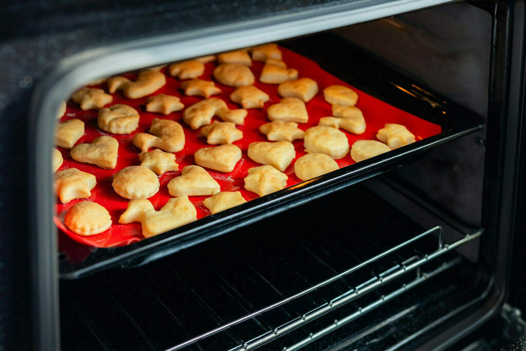 Sweet tasty delicious curd ginger cookies baking in hot oven stove on tray and red bright silicone bakery mat at home kitchen. Homemade hot biscuits making process.